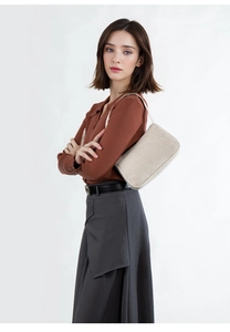 Close-up of a stylish champagne leather underarm bag worn with a brown knit sweater