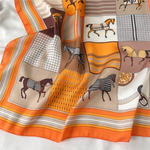 Close-up of luxury silk scarf with orange horse motifs and geometric satin texture