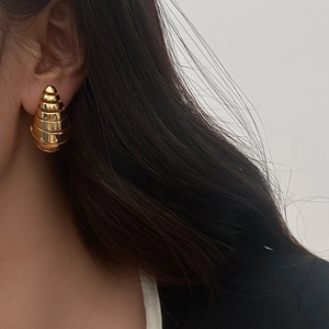 Gros plan de boucles d'oreilles spirales dorées texturées portées par un mannequin femme