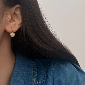 Gros plan de boucles d'oreilles cœur dorées avec zircons portées par le modèle