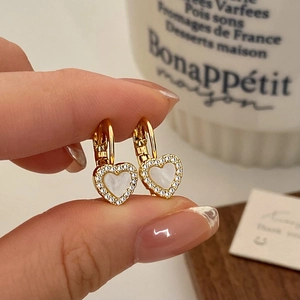 Élégantes boucles d'oreilles cœur en or avec nacre blanche et zircons sur la main