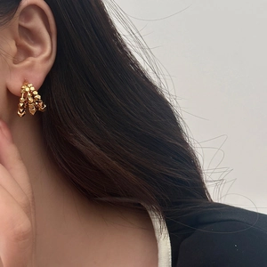 Detail of layered gold geometric earrings shown on ear with a metallic faceted texture