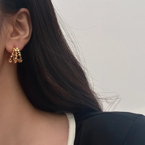 Close-up of golden cluster stud earrings with geometric metal beads on a female model