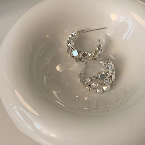 Detailed view of silver C-shaped hoop earrings with faceted geometric metallic texture