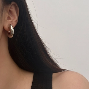 Gros plan sur une boucle d'oreille créole argentée épaisse en C portée par un mannequin