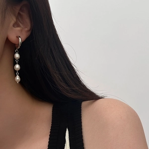 Detail of three Baroque pearls cascading from a silver hoop earring worn by a model