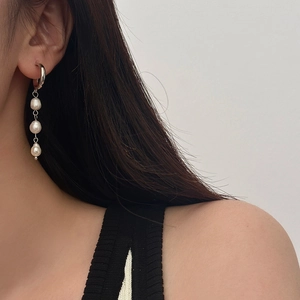 Detail of silver drop earrings featuring long metal chains and three baroque pearls