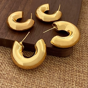 Deux paires de boucles d'oreilles créoles dorées en forme de C sur un socle