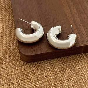 Détail de boucles d'oreilles créoles argentées en C sur fond bois et jute