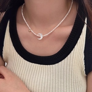 Détail d'un collier de perles avec pendentif croissant de lune et breloque en zircon