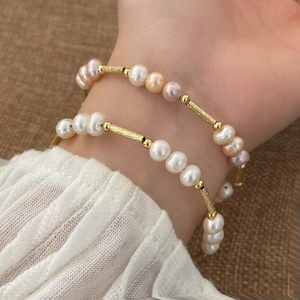Detail eines Naturperlen-Armbands mit goldenen Metallröhren am Handgelenk getragen