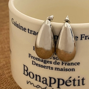 Dettaglio degli orecchini a goccia in metallo argentato appesi a una tazza bianca