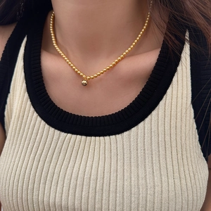 Close-up of a gold-plated beaded necklace with a small round pendant on model