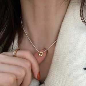 Minimalist circular pendant necklace and geometric ring styled on a cream knit sweater