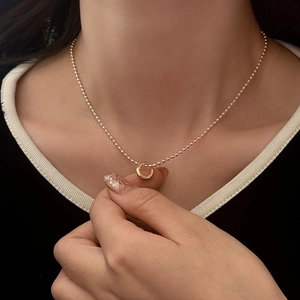 Close-up of a minimalist gold ring pendant on a bead chain necklace worn by a model