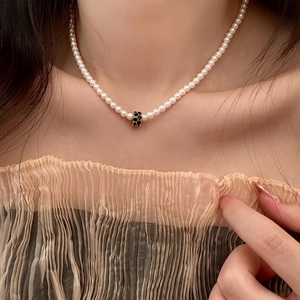 Détail d'un collier de perles élégant avec pendentif cylindre pavé noir sur le cou