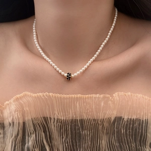 Gros plan du collier de perles avec perle centrale dorée et cristaux noirs sur le cou