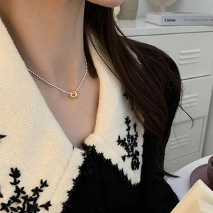 Close-up of minimalist gold ring pendant on a silver bead chain necklace worn by a model