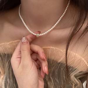 Vue détaillée d'un collier de perles élégant avec un pendentif cylindrique doré serti
