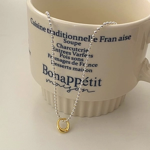 Minimalist silver bead necklace with a gold ring pendant displayed on a beige mug