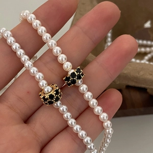 Détail d'un collier de perles blanches avec perle dorée ajourée et cristaux noirs