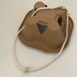 Détail d'un collier de perles élégant avec perle pavée dorée sur plateau rustique