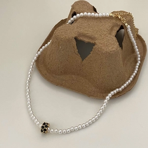 Détail du collier de perles blanches avec pendentif cylindre doré et cristaux noirs