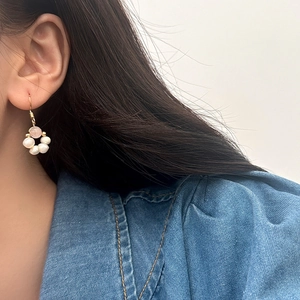 Detail of pink gemstone and white freshwater pearl dangling earrings worn by a model