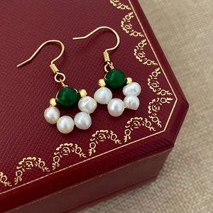 Detailed close-up of gold drop earrings with green jade beads and freshwater pearls