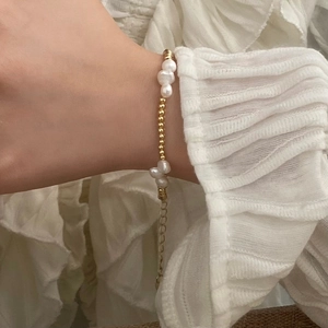 Close-up of elegant freshwater pearl bracelet with gold beads on a white chiffon sleeve