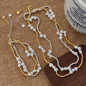 Detail of baroque pearl and metal bead necklace with heart charm on rustic linen background