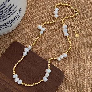 Detail of natural freshwater pearl necklace with gold beads and heart charm on linen