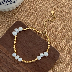 Detailed view of baroque pearl bracelet with gold beads and heart charm on wood