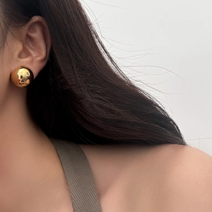 Close-up of high-polished gold spherical stud earrings on model for a minimalist chic look