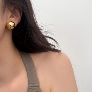 Macro shot of polished gold spherical stud earring with minimalist mirror finish design