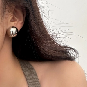 Macro shot of high-polish silver metal ball earring on model showing sleek mirror finish