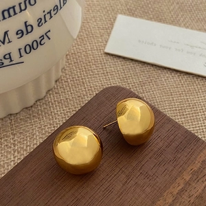 Polished gold-plated dome stud earrings displayed on a rustic wood and fabric surface