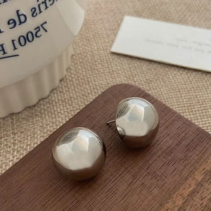 Detailed view of polished metal sphere stud earrings on a minimalist wooden display