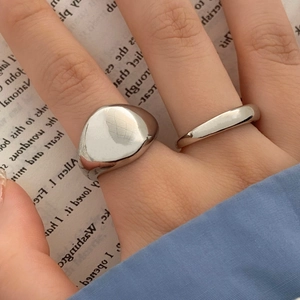 Close-up of minimalist silver signet ring and thin band worn on hand over book