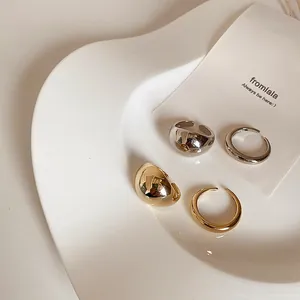 Polished gold and silver minimalist open rings displayed on a white ceramic wave tray