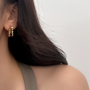 Detail of gold geometric hoop earrings with faceted metallic texture on model