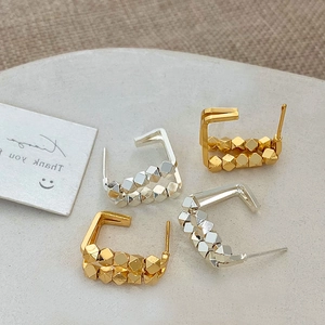 Close-up of geometric square hoop earrings in gold and silver finish on display stand