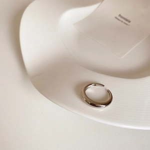 Detailed close-up of a minimalist silver open ring on a clean ceramic display tray