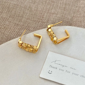 Detail of gold C-shaped hoop earrings with geometric beads on a stone tray