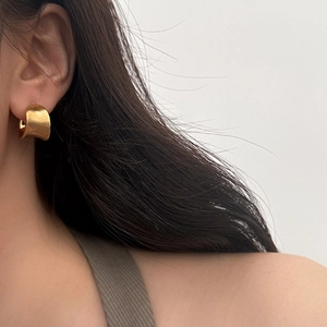 Macro shot of minimalist gold plated C-shaped wide earrings with brushed metal texture