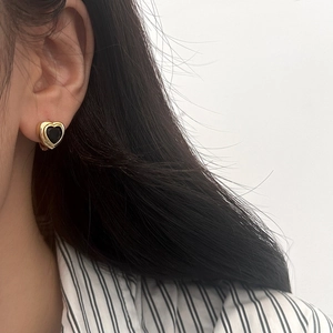 Gros plan d'un modèle portant des boucles d'oreilles cœur dorées et zircon noir vintage