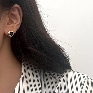 Gros plan d'un modèle portant des boucles d'oreilles cœur noir vintage avec bordure dorée