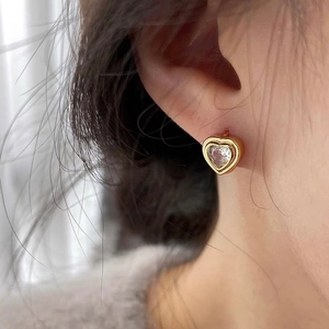 Gros plan d'une boucle d'oreille cœur dorée avec zircon étincelant portée sur l'oreille