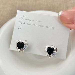 Vue macro de boucles d'oreilles cœur argentées avec zircon noir sur carte blanche