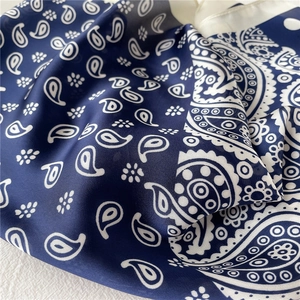 Gros plan d'un foulard carré en soie bleu marine avec motifs paisley et texture satinée